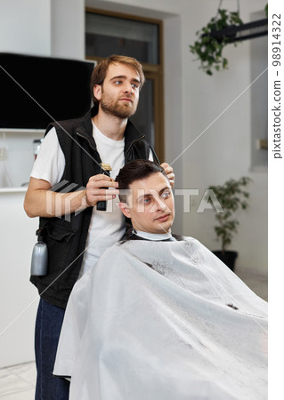 Barber shaving caucasian man in barber shop. 98914322