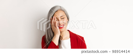 Beauty and makeup concept. Close up of beautiful asian mature woman, laughing and touching face, smiling happy, standing over white background Beauty and makeup concept. Close up of beautiful asian mature woman, laughing and touching face, smiling happy, standing over white background 98914414