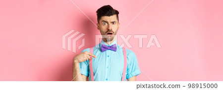 Image of confused funny guy in bow-tie and suspenders, pointing at himself as if being accused or chosen, raising eyebrow surprised, standing over pink background Image of confused funny guy in bow-tie and suspenders, pointing at himself as if being accused or chosen, raising eyebrow surprised, standing over pink background 98915000