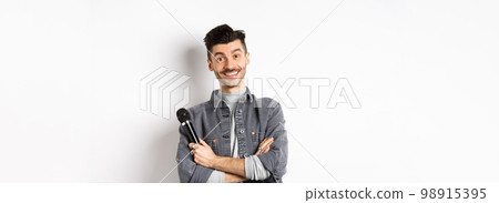 Handsome caucasian guy with moustache cross arms on chest, holding mic and smiling at camera, perform on stage with microphone, standing against white background Handsome caucasian guy with moustache cross arms on chest, holding mic and smiling at camera, perform on stage with microphone, standing against white background 98915395