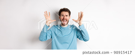 Image of freaked out young man screaming and shaking hands, shouting at camera frustrated or worried, panicking over white background Image of freaked out young man screaming and shaking hands, shouting at camera frustrated or worried, panicking over white background 98915417