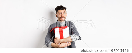 Excited man hugging romantic gift for girlfriend, waiting for valentines date with lover, looking at empty space logo with happy face, standing on white background Excited man hugging romantic gift for girlfriend, waiting for valentines date with lover, looking at empty space logo with happy face, standing on white background 98915466