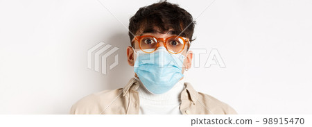 Coronavirus pandemic and healthy people concept. Surprised guy in glasses and face mask raising eyebrows, stare at camera in awe, standing on white background Coronavirus pandemic and healthy people concept. Surprised guy in glasses and face mask raising eyebrows, stare at camera in awe, standing on white background 98915470