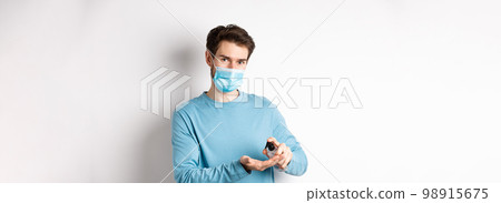 Covid-19, health and quarantine concept. Caucasian man in medical mask using hand sanitizer, apply antiseptic from coronavirus spread, white background 98915675