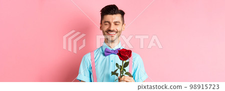 Valentines day and romance concept. Romantic man with red rose going on date with lover, standing in fancy bow-tie on pink background 98915723
