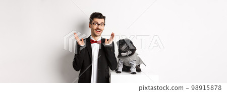Animals, party and celebration concept. Handsome man and cute dog in costumes suits staring surprised at camera, reacting on promo offer amazed, white background Animals, party and celebration concept. Handsome man and cute dog in costumes suits staring surprised at camera, reacting on promo offer amazed, white background 98915878