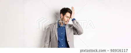 Annoyed businessman in suit facepalm with eyes closed, bothered by someone stupid, pissed-off at work, standing on white background 98916117