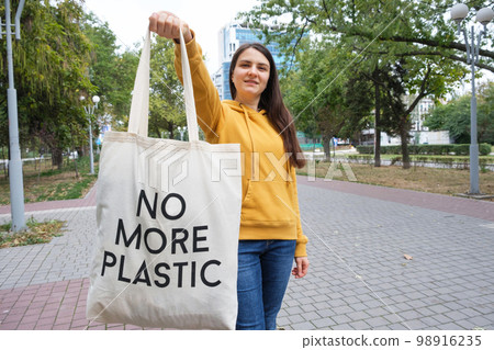A woman shows a fabric reusable bag with the text no more plastic. A woman shows a fabric reusable bag with the text no more plastic. 98916235