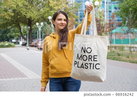 A woman shows a fabric reusable bag with the text no more plastic. A woman shows a fabric reusable bag with the text no more plastic. 98916242