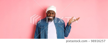 Annoyed and pissed-off african-american man pointing finger at head, scolding someone stupid, staring bothered at camera, pink background 98916257
