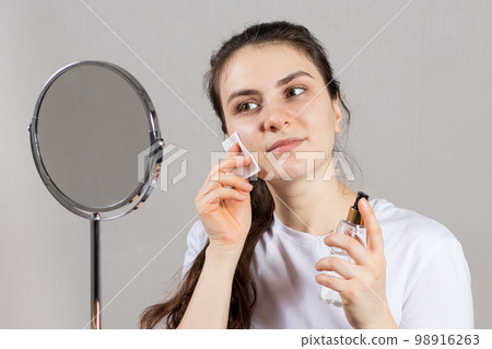 A 25-year-old woman holds a face and neck tonic and a cotton pad. Anti-wrinkle skin care, vitamins and acids for the face. A 25-year-old woman holds a face and neck tonic and a cotton pad. Anti-wrinkle skin care, vitamins and acids for the face. 98916263