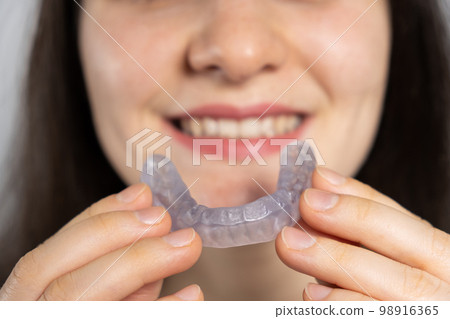 A woman holds dental mouthguard, splint for the treatment of dysfunction of the temporomandibular joints, bruxism, malocclusion, to relax the muscles of the jaw. 98916365