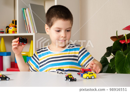 A preschool child plays with toy cars sitting at a table at home. A preschool child plays with toy cars sitting at a table at home. 98916551