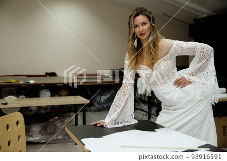 A girl in a boho wedding dress in a sewing workshop. 98916591