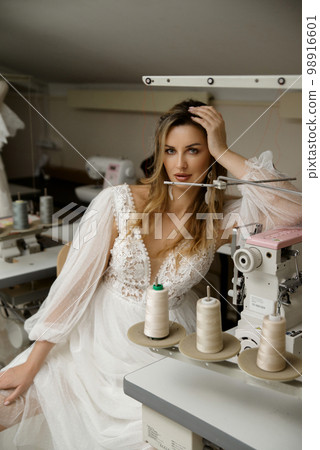 A girl in a boho wedding dress in a sewing workshop. 98916601