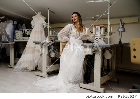 A girl in a boho wedding dress in a sewing workshop. 98916627