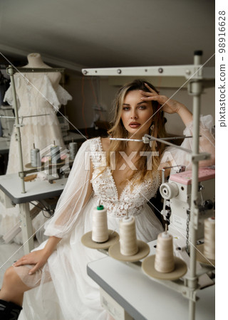 A girl in a boho wedding dress in a sewing workshop. 98916628
