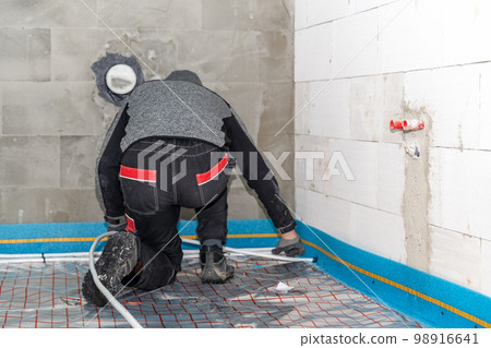 a worker installs underfloor heating in a new building 98916641