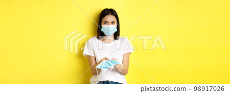Coronavirus, quarantine and medicine concept. Angry asian girl giving you medical mask indoors, frowning upset, standing over yellow background Coronavirus, quarantine and medicine concept. Angry asian girl giving you medical mask indoors, frowning upset, standing over yellow background 98917026