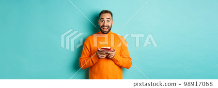 Happy adult man celebrating birthday, holding bday cake with candle and smiling, standing against turquoise background Happy adult man celebrating birthday, holding bday cake with candle and smiling, standing against turquoise background 98917068