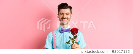 Happy man showing tongue and smiling, holding red rose for girlfriend on Valentines day, enjoying romantic date, pink background Happy man showing tongue and smiling, holding red rose for girlfriend on Valentines day, enjoying romantic date, pink background 98917125
