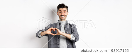 Smiling boyfriend showing heart with love, looking romantic and happy at lover, standing on white background. Valentines day and relationship concept Smiling boyfriend showing heart with love, looking romantic and happy at lover, standing on white background. Valentines day and relationship concept 98917163