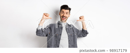 Handsome and confident man smiling, pointing at himself, self-promoting and feeling like professional, standing on white background Handsome and confident man smiling, pointing at himself, self-promoting and feeling like professional, standing on white background 98917179