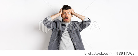 Alarmed young man grab head and pop eyes at camera, looking worried and troubled, having big problem, panicking on white background Alarmed young man grab head and pop eyes at camera, looking worried and troubled, having big problem, panicking on white background 98917363
