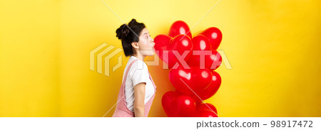 Valentines day and relationship concept. Profile of young asian woman scream of surprise, say wow and looking left amazed, standing near red balloons, yellow background Valentines day and relationship concept. Profile of young asian woman scream of surprise, say wow and looking left amazed, standing near red balloons, yellow background 98917472