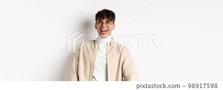 Image of happy young man laughing and looking upbeat, watching something funny, standing on white background 98917598