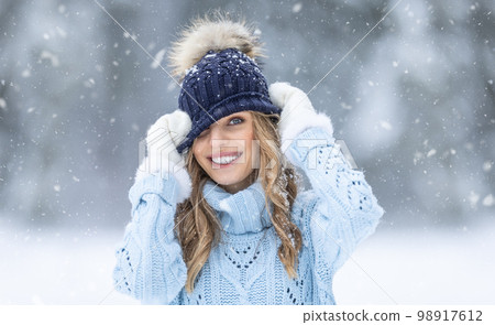 A cute young woman is enjoying the winter and snow, putting on a hat in a very funny way 98917612