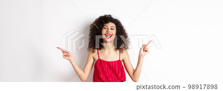 Happy beautiful lady in red dress, laughing and pointing sideways, showing two ways, standing on white background Happy beautiful lady in red dress, laughing and pointing sideways, showing two ways, standing on white background 98917898