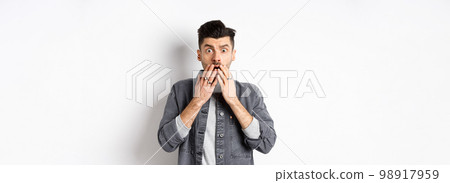 Shocked caucasian guy gasping alarmed, cover mouth with hands and staring at something terrible, witness bad accident, say oh my god, standing on white background Shocked caucasian guy gasping alarmed, cover mouth with hands and staring at something terrible, witness bad accident, say oh my god, standing on white background 98917959