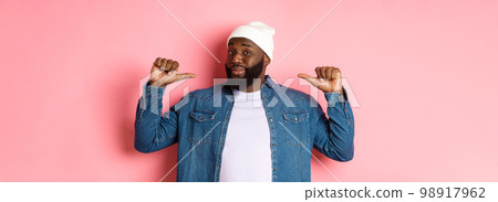 Confident and cheeky Black man pointing at himself, staring at camera self-assured, show-off, standing over pink background Confident and cheeky Black man pointing at himself, staring at camera self-assured, show-off, standing over pink background 98917962