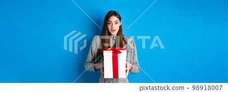 Valentines day concept. Surprised happy girl receiving romantic gift and looking thankful at camera, standing on blue background Valentines day concept. Surprised happy girl receiving romantic gift and looking thankful at camera, standing on blue background 98918007