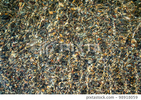 The texture of the bottom. Many small stones are visible under the clear water. Water ripples of the sea, sun rays on the rocks. The texture of the bottom. Many small stones are visible under the clear water. Water ripples of the sea, sun rays on the rocks. 98918059