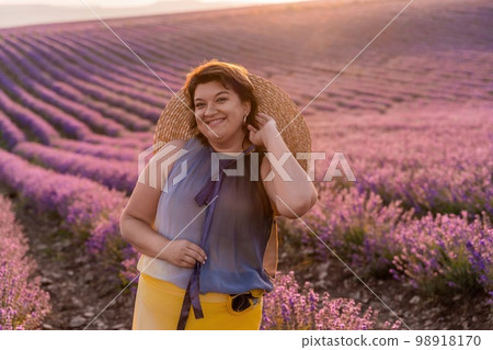 Woman lavender field sunset. Romantic woman walks through the lavender fields. illuminated by sunset sunlight. Dressed in a dress with a hat. 98918170