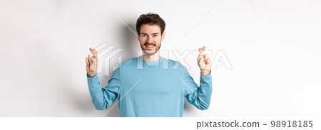 Optimistic smiling man cross fingers for good luck, making wish and waiting for results, standing over white background Optimistic smiling man cross fingers for good luck, making wish and waiting for results, standing over white background 98918185