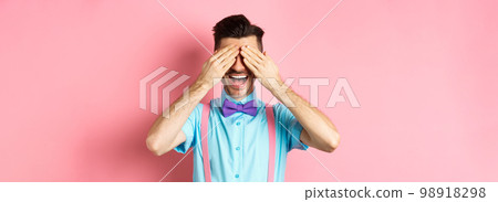 Cheerful young man celebrating, waiting for surprise with closed eyes and happy smile, standing joyful on pink background Cheerful young man celebrating, waiting for surprise with closed eyes and happy smile, standing joyful on pink background 98918298