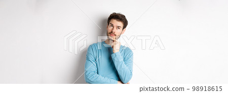 Image of handsome young man making choice, thinking and looking pensive up, standing over white background Image of handsome young man making choice, thinking and looking pensive up, standing over white background 98918615