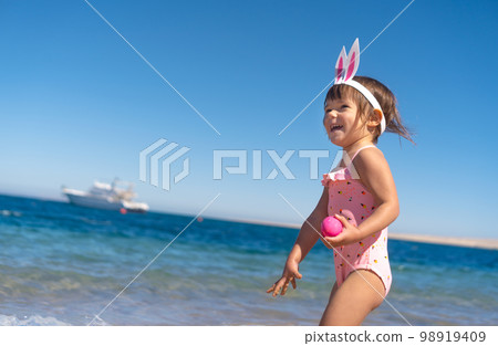 Toddler girl with easter eggs on the beach  98919409