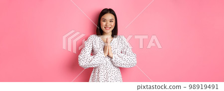 Beautiful asian woman thanking you, holding hands together in appreciation gesture, smiling happy at camera, standing grateful over pink background Beautiful asian woman thanking you, holding hands together in appreciation gesture, smiling happy at camera, standing grateful over pink background 98919491