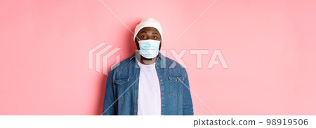 Covid-19, lifestyle and quarantine concept. Happy Black guy in beanie and face mask smiling with eyes, standing over pink background 98919506