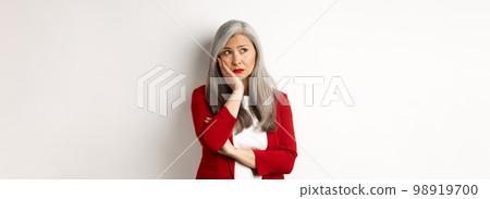 Troubled and sad asian female entrepreneur looking at upper left corner, thinking with upset face, standing over white background 98919700