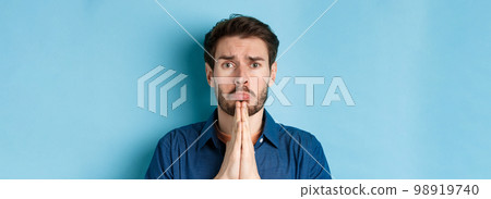 Sad young man begging for help, apoligizing and sobbing miserable, standing on blue background 98919740