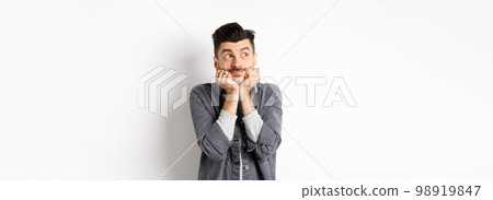 Excited cute young man look dreamy at upper left corner, waiting for parcel, daydreaming or imaging something, standing on white background 98919847