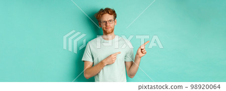 Judgemental redhead man in glasses grimacing, frowning disappointed and pointing left, showing bad promo offer, standing over turquoise background Judgemental redhead man in glasses grimacing, frowning disappointed and pointing left, showing bad promo offer, standing over turquoise background 98920064
