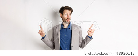Indecisive male entrepreneur in suit pointing fingers sideways, choosing between two variants, looking at left logo pensive, standing on white background Indecisive male entrepreneur in suit pointing fingers sideways, choosing between two variants, looking at left logo pensive, standing on white background 98920113