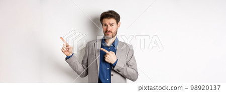 Showing bad example. Skeptical businessman look displeased and frowning while pointing at upper right corner banner, standing against white background 98920137