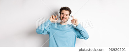 Handsome man listening music in wireless headphones and smiling, enjoying good sound, white background 98920201